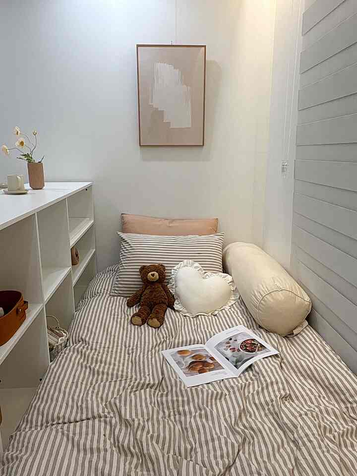 ナチュラルなベージュとホワイトの色調の寝室、ストライプの寝具と多様なクッションが配置された印象的な空間