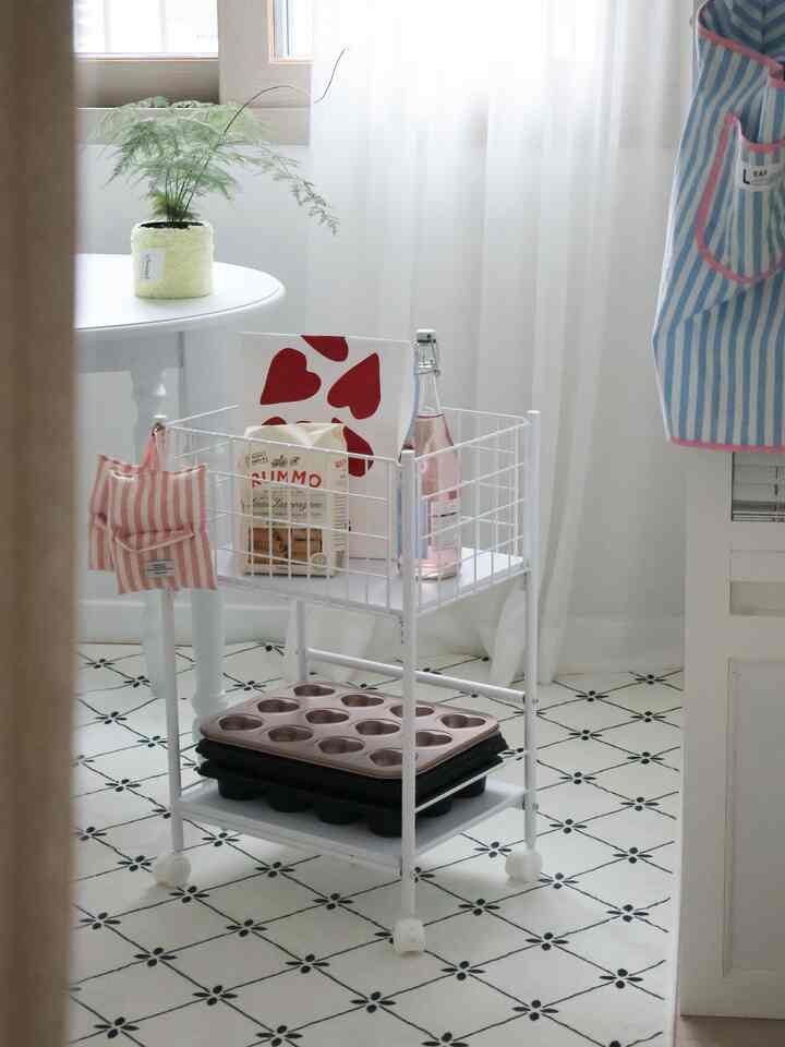 White-toned kitchen space featuring a baking supplies storage trolley, round table, and patterned rug with cozy atmosphere