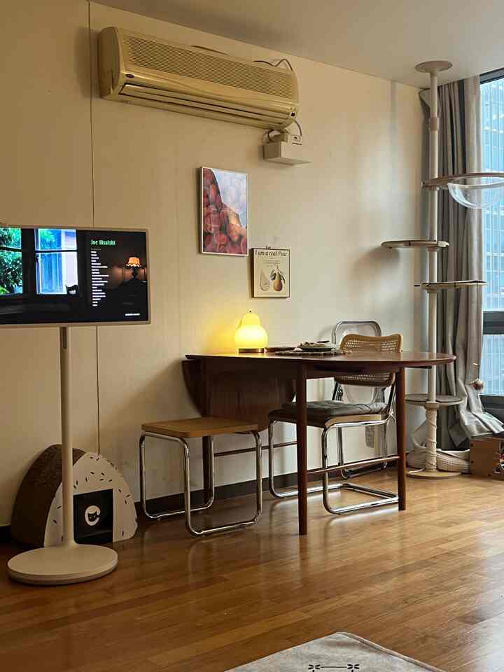 白い壁とブラウンの木製床が調和するリビング、大きな窓際にダイニングテーブルと猫用タワーが配置された自然な雰囲気のインテリア