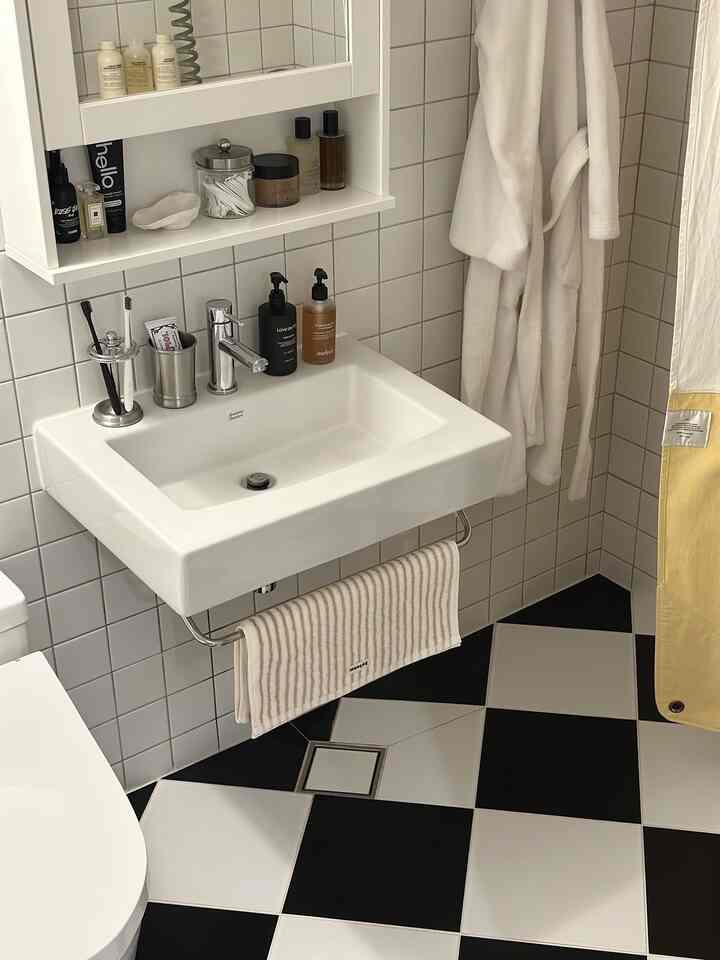 Clean bathroom with white sink and towel, black and white tiled floor, white hooded robes hanging on wall, neat atmosphere