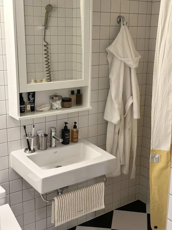 ホワイトとグレーのトーンのコンパクトなバスルーム、洗面台と清潔なタオル、バスローブが配置されたミニマルな雰囲気のインテリア