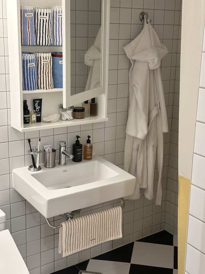 A white and gray toned bathroom featuring a clean sink and neatly organized towel storage, showcasing a minimal and modern design.