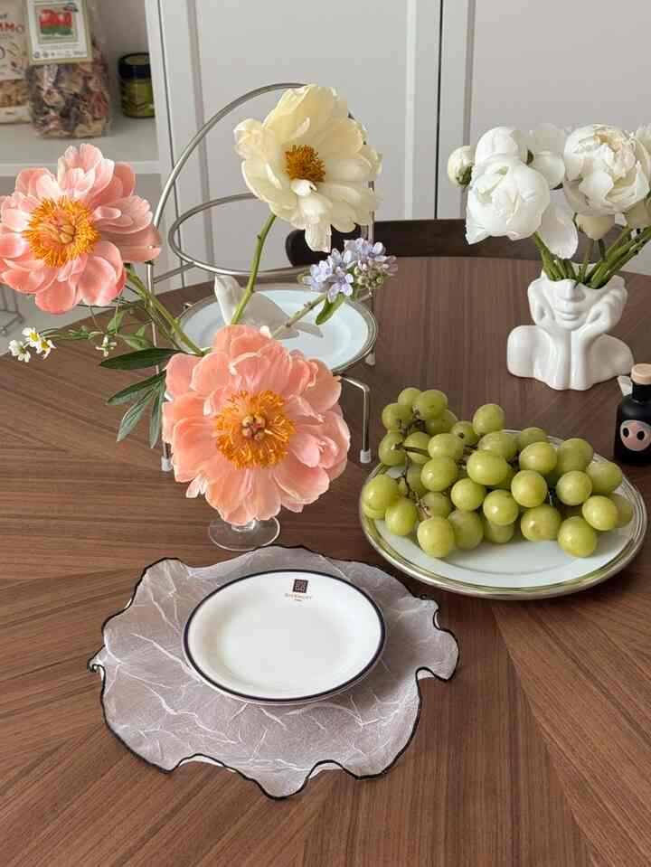 ブラウンの木目調テーブルに白い皿や華やかな花瓶、ぶどうが置かれたシンプルでモダンなダイニング空間