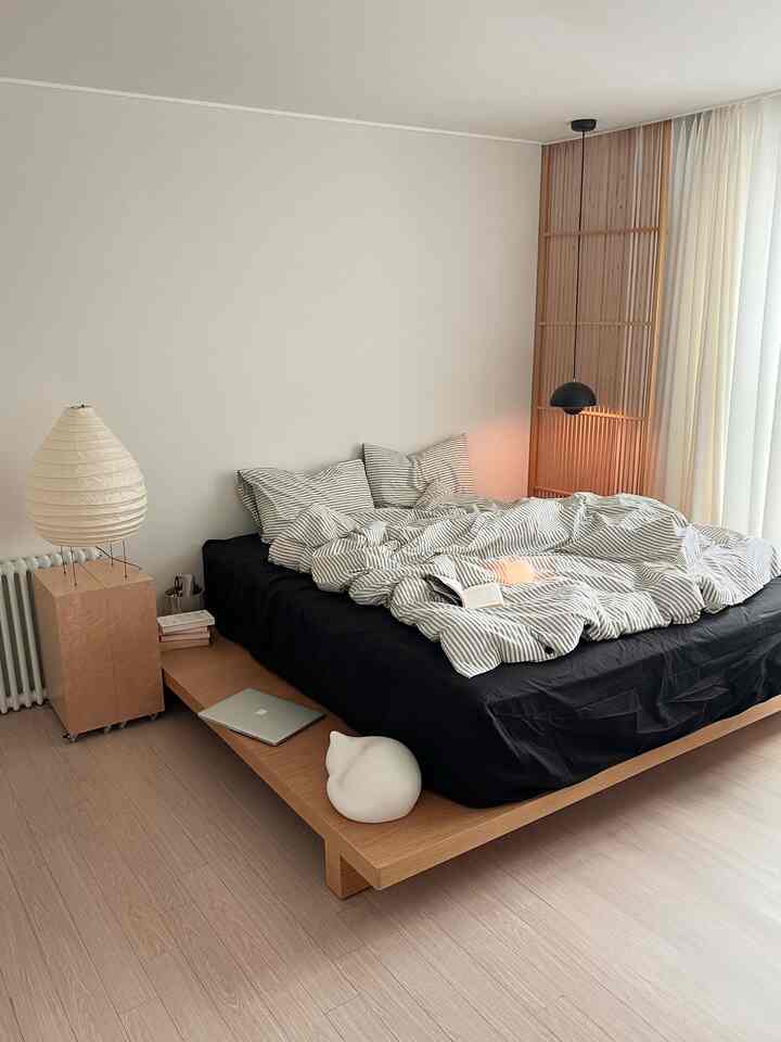 Modern bedroom with white walls, wood tone flooring, black bed frame and striped bedding
