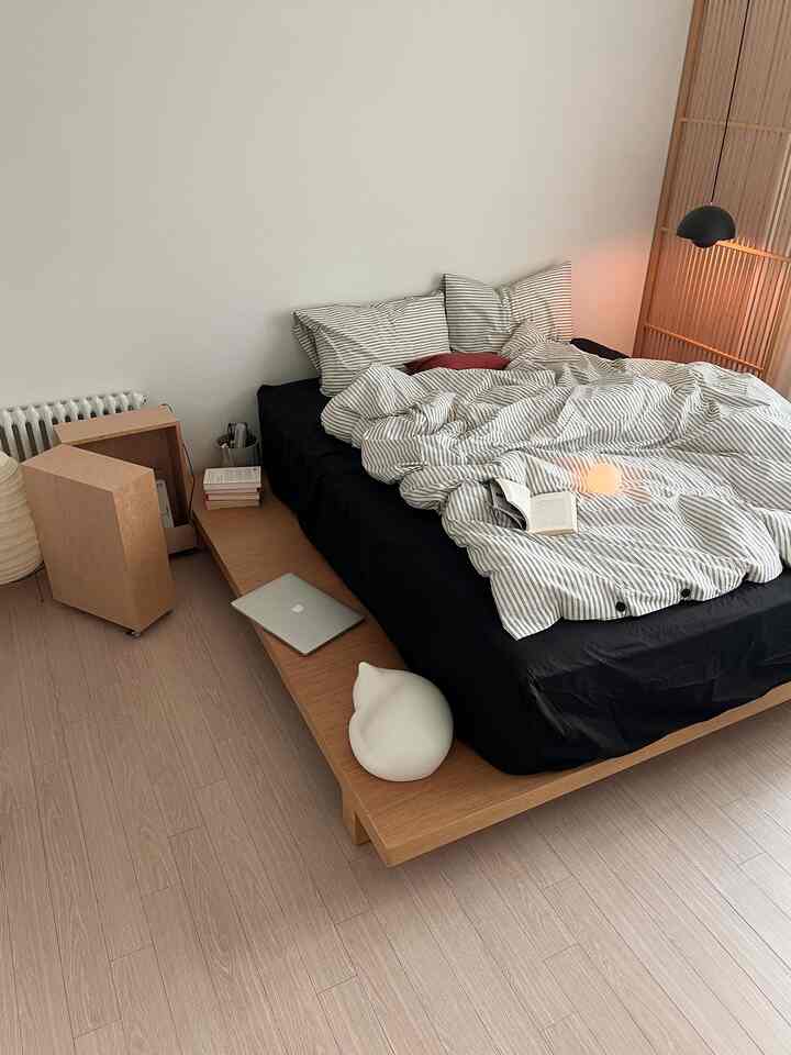 A natural modern bedroom with wood tone flooring and bed platform, featuring black bedding for a cozy atmosphere