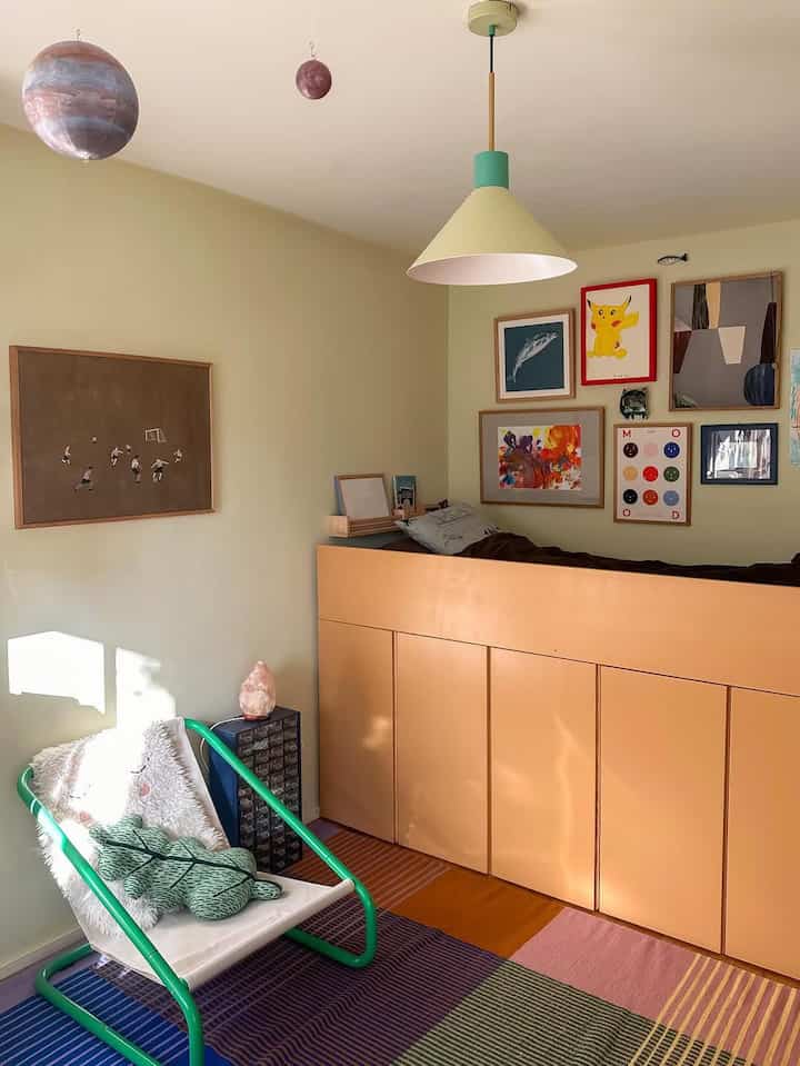 Beige-toned kids' room featuring green armchair and colorful wall decor in a cozy loft space