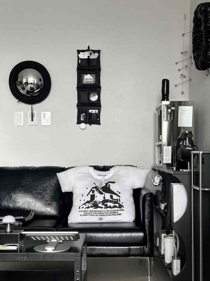 グレーの壁、黒のレザーソファ、金属製の棚とモビールが配置されたモダンなリビングルーム