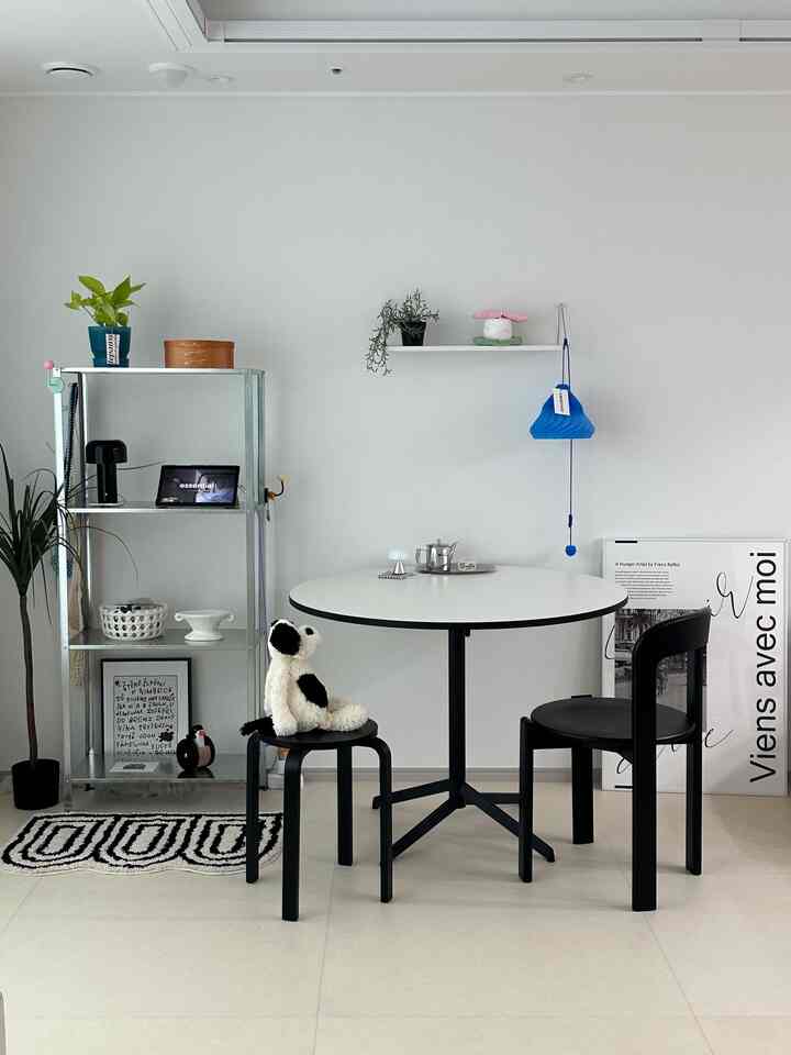 白い壁と床のモノトーンリビング、中央に配置された黒の円形テーブルと椅子、スツールがあるシンプルモダンなホームカフェ空間