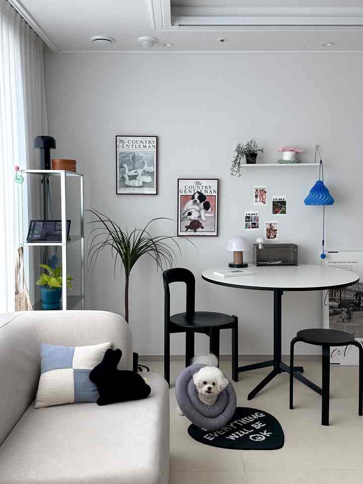 明るいホワイトとブラックの色調が調和したリビング、丸テーブルと黒い椅子、ヴィンテージ額装アートが配置されたモダンなおうちカフェ空間