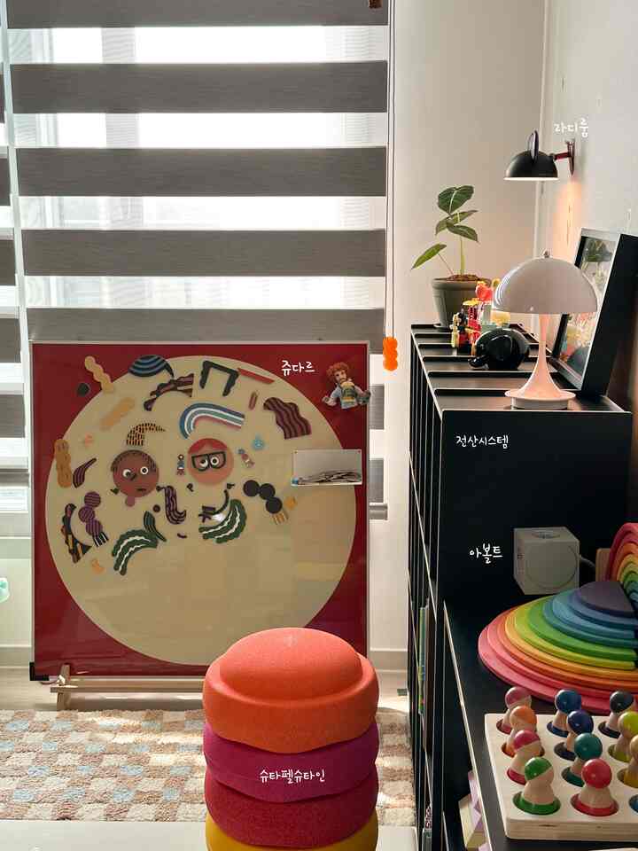 明るいグレーのブラインドを背景に、カラフルなおもちゃと積み重ねられたスツールが配置された印象的な子供部屋