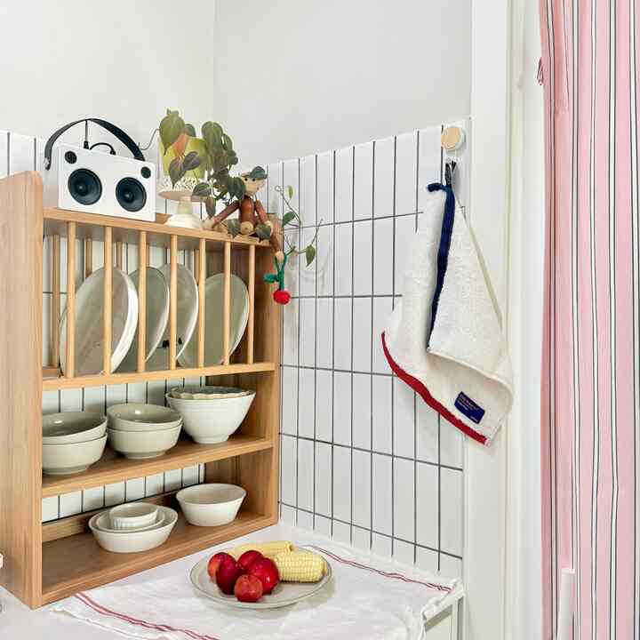 白いタイルとナチュラルな木製棚が配置されたキッチン、皿とタオルが整然とした雰囲気のあるインテリア