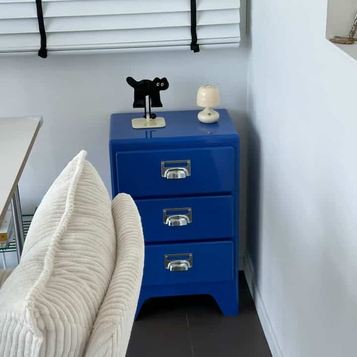 白い壁とクッション付きのソファがある空間に、青い3段の引き出し棚が配置された清潔感のあるリビング