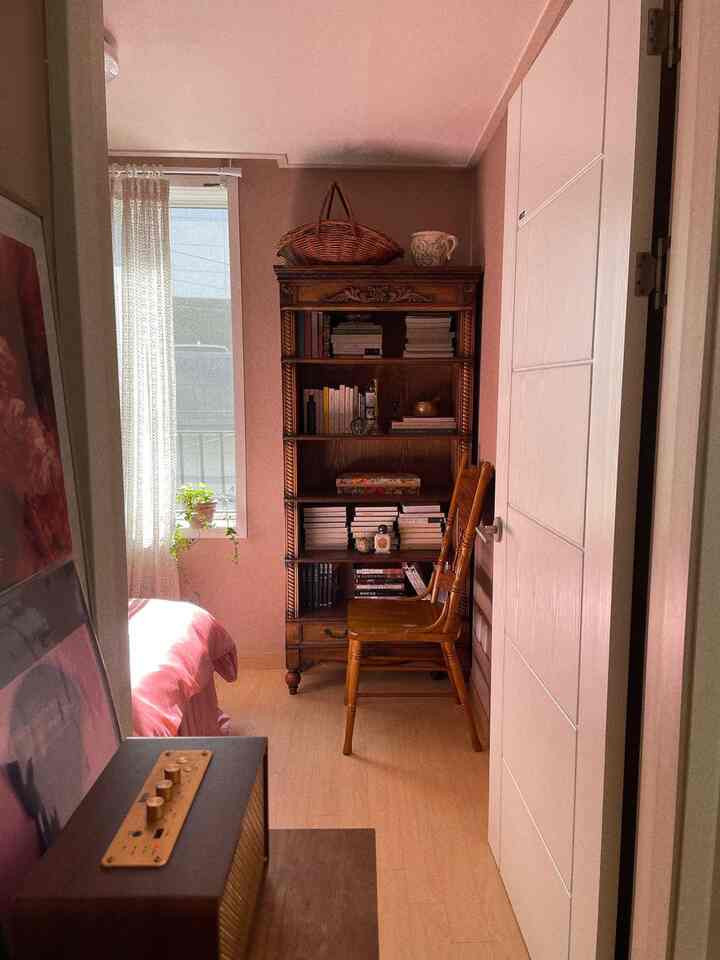 暖かいベージュトーンの狭い寝室、木製の本棚と椅子が配置されたヴィンテージな雰囲気のあるインテリア