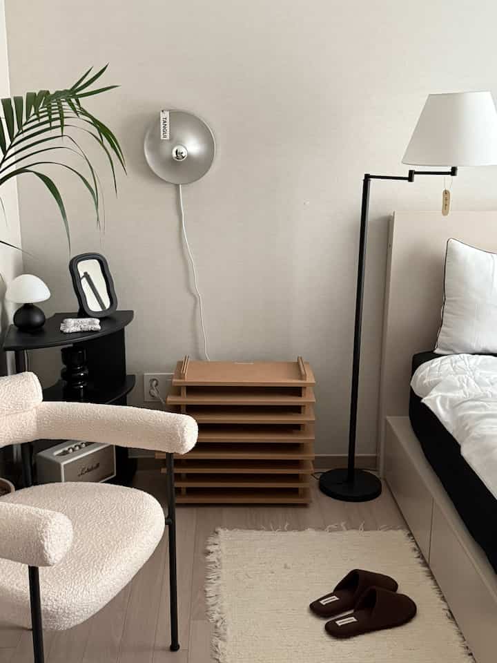 Beige-toned bedroom featuring bed, boucle armchair, and black floor lamp in a modern setting