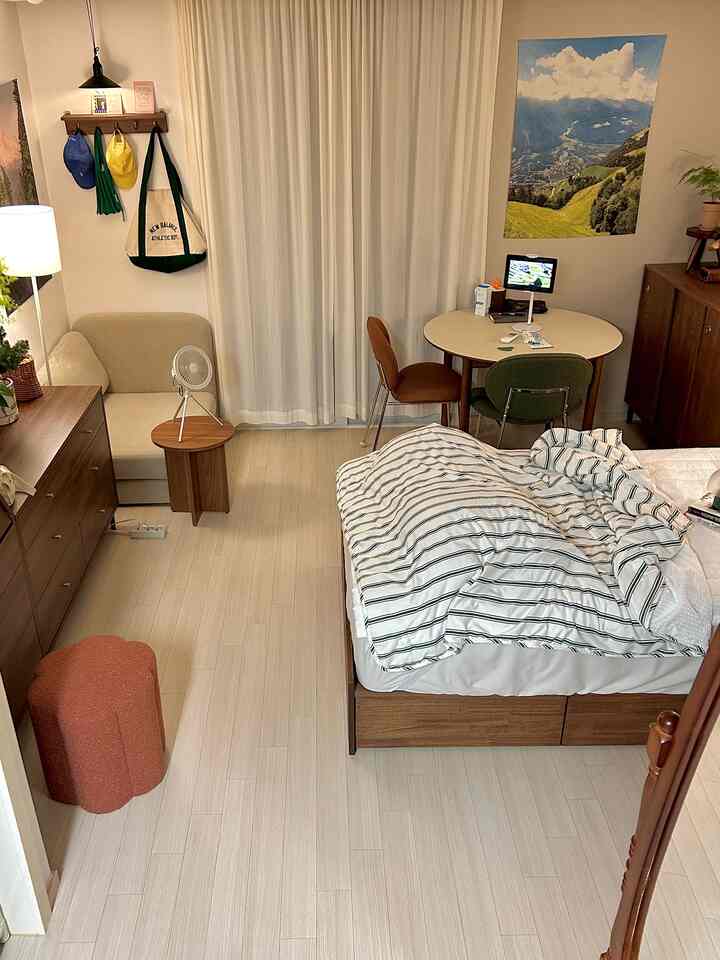 ナチュラルなウッドトーンのワンルーム、一人暮らし向けのベッドと丸いダイニングテーブル、ソファベッドが配置された居心地の良い空間