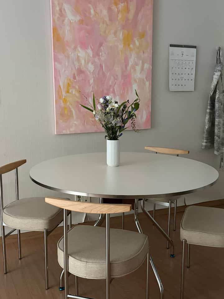 A simple modern dining room in white and wood tones featuring a round dining table, four chairs, and a vase with flowers