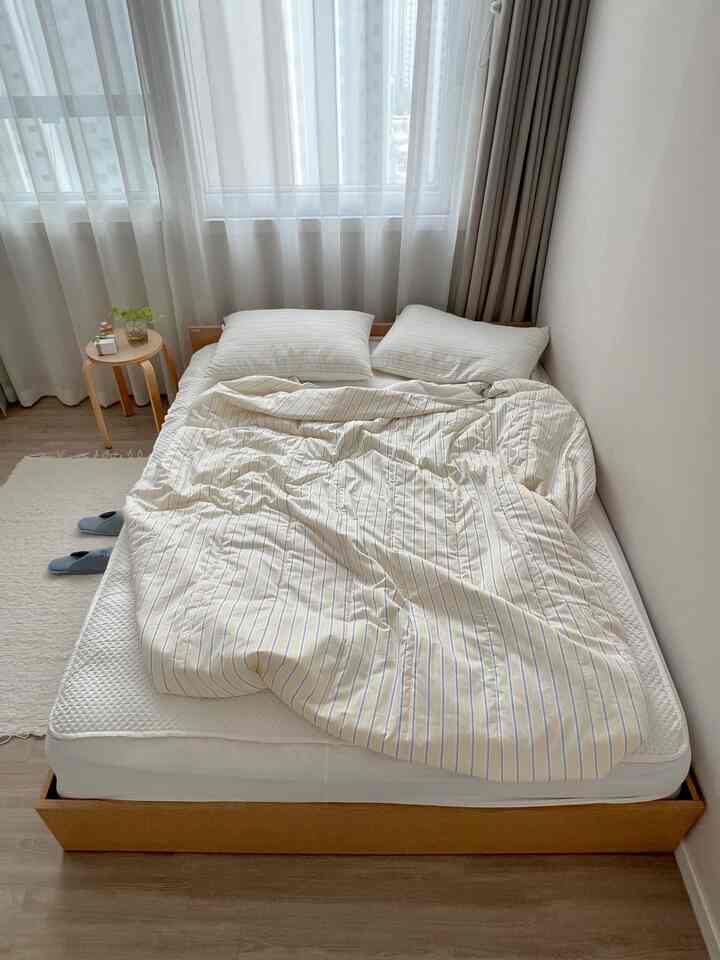 明るくナチュラルな雰囲気の寝室、低床ベッドと木製スツールが配置された印象的な空間