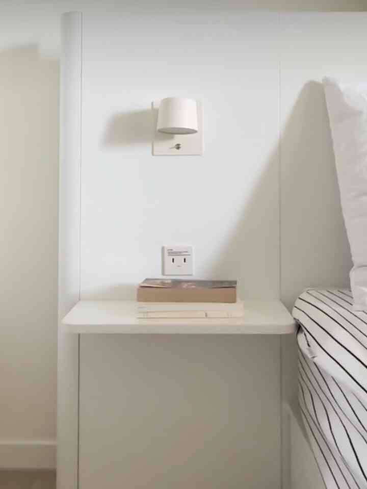 White-toned bedroom nightstand with striped bedspread in a simple, clean space