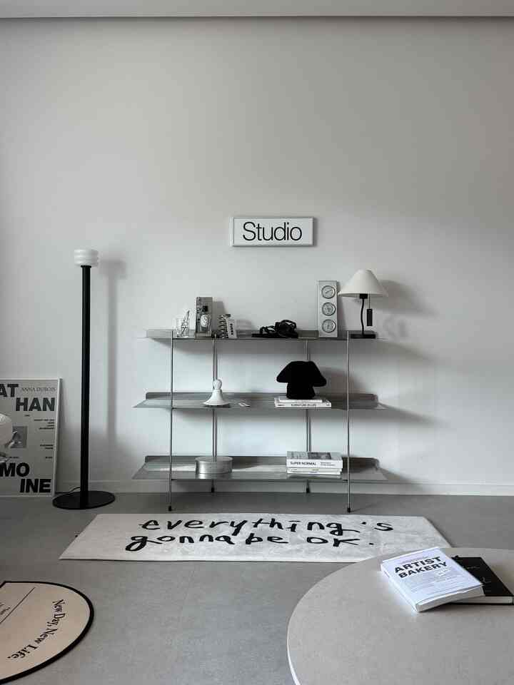 モノトーンのリビング、ステンレス棚と黒のフロアランプが配置されたシンプルで落ち着いた空間