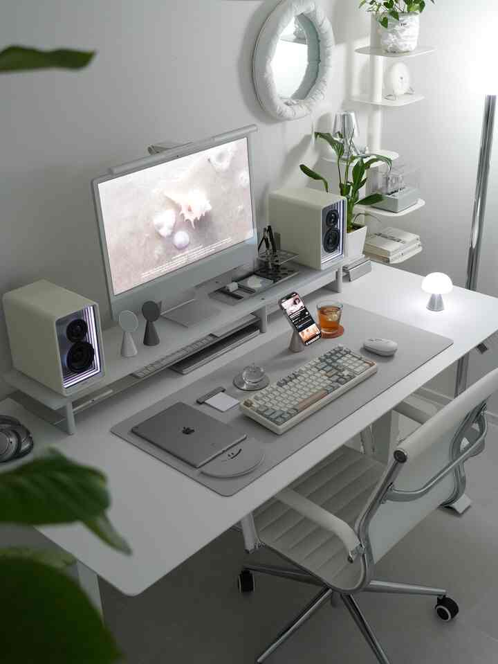White-toned study space featuring a neat desk with monitor, keyboard, and phone stand, creating a modern and organized atmosphere