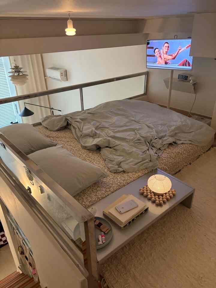 暖かいベージュトーンのロフト寝室、中央にベージュのマットレスと枕が配置されたモダンな空間