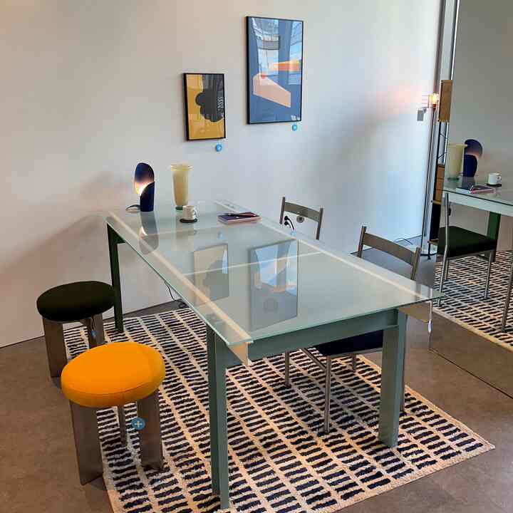 Dining room in green and navy tones featuring a modern glass dining table, stools, and lighting in a clean setting