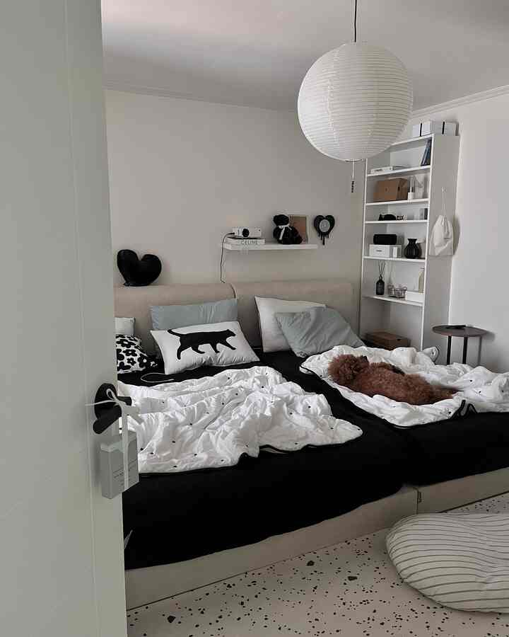 A white and monotone bedroom featuring two central beds and a bookshelf, with a dog lying on one bed creating a cozy atmosphere