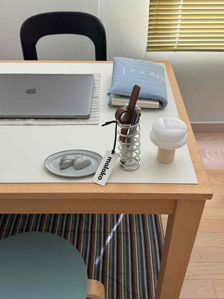 白とナチュラルウッドトーンの一人用ホームオフィス、整ったデスクとスツールにノートパソコンとテーブルランプが置かれたモダンな雰囲気のインテリア