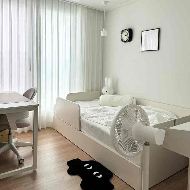 白と木目調の組み合わせの子供部屋、ベッドとデスク、柔らかいカーテンが配されたシンプルで清潔感のあるインテリア