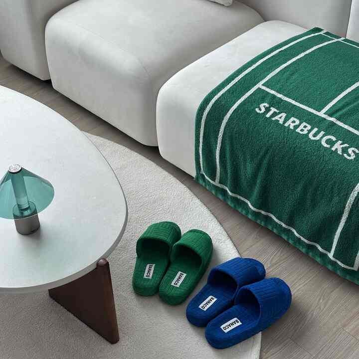 A simple and cozy living room in white and green tones featuring a sofa, rug, and living room slippers