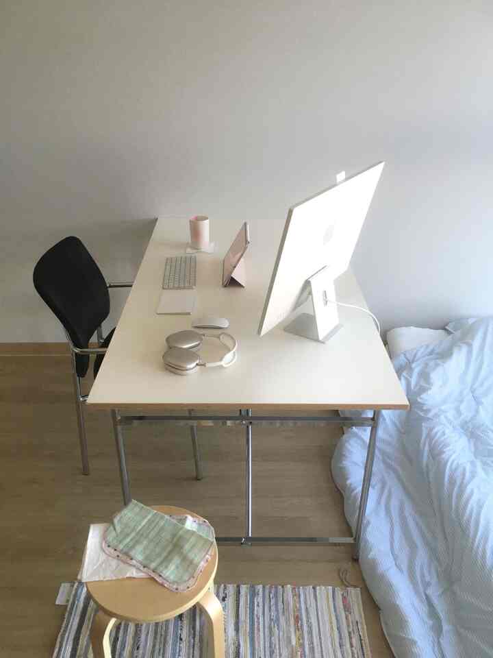 White and wood tone studio bedroom featuring a simple desk and armchair in a minimal remote work setup