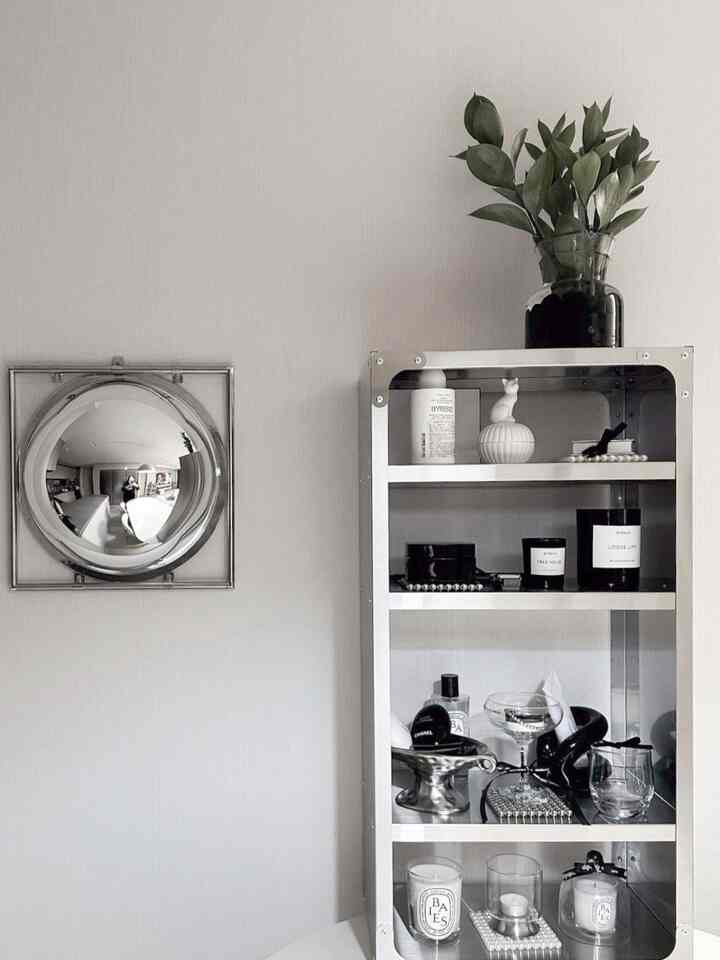 Monotone space featuring stainless steel rack with plants and scented candles on a white wall background