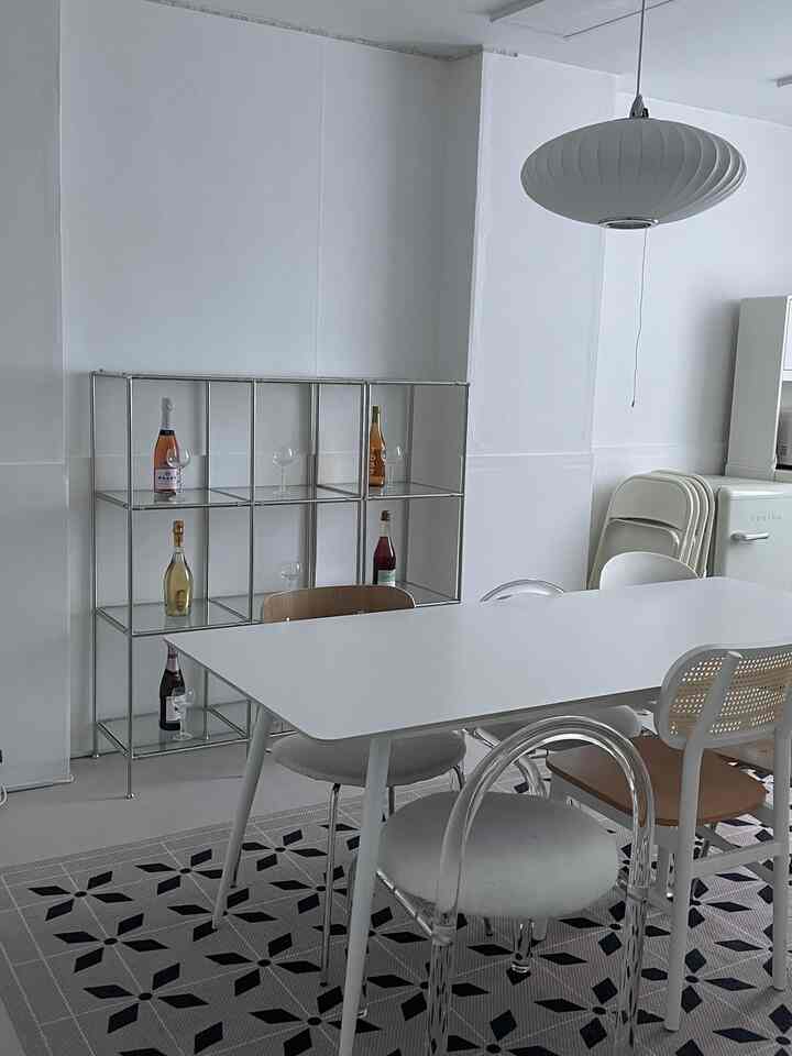 White-toned kitchen featuring a spacious ceramic dining table, mixed chairs, and large patterned rug in a simple modern style