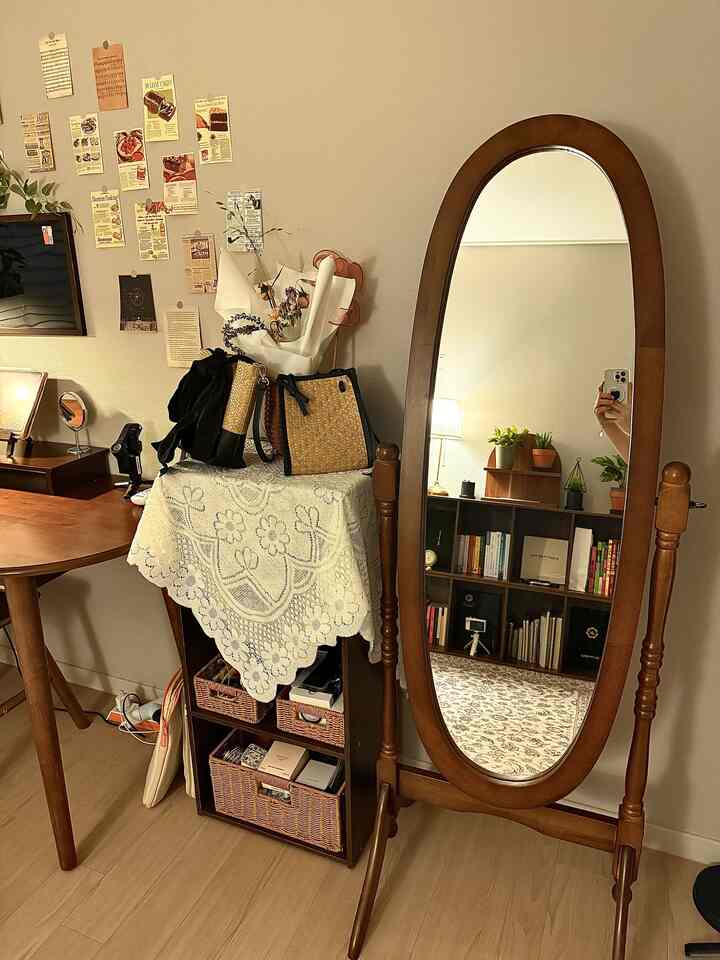 暖かいブラウンの木目調が印象的なリビング、全身鏡と丸テーブル、本棚が配置された雰囲気のある空間