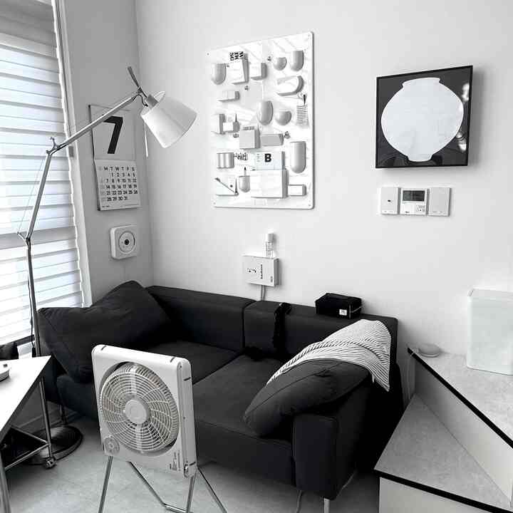 モノトーンの黒と白のリビング、黒いソファと白いフロアランプ、月壺の額縁が配置されたシンプルで印象的なインテリア