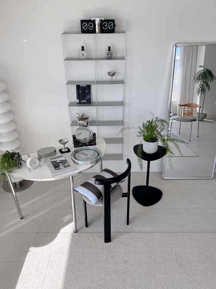 A clean and modern living room with white walls and floor featuring a black chair, side table, and green plants