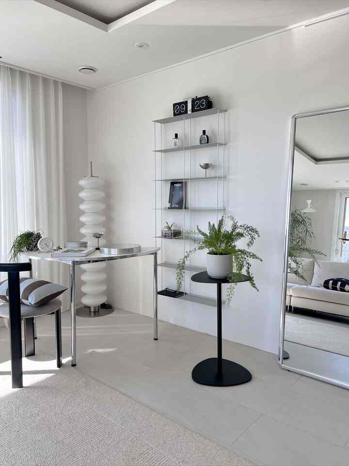White-toned living room featuring a mid-century modern metal table, large mirror, plants, and minimalist furniture arrangement creating a clean interior