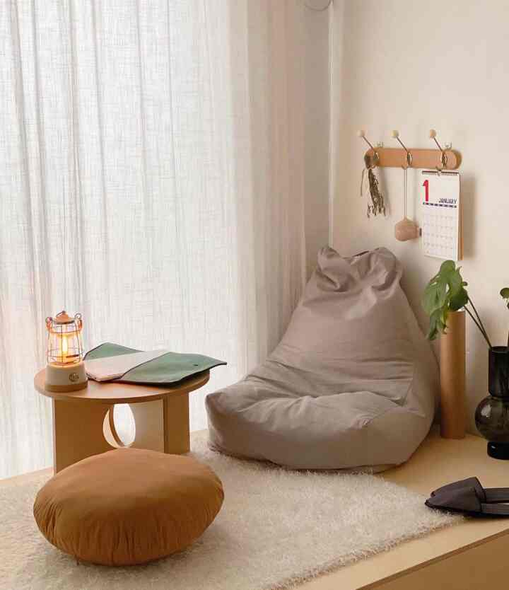 Beige and wood-toned kids' room featuring a bean bag, round side table, and sheer curtains creating a simple, cozy atmosphere