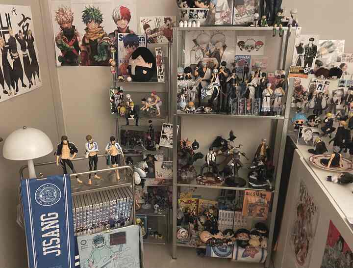 ベージュや中間色のトーンのオタク部屋、マンガのフィギュアが棚にぎっしり並び、関連するポスターが壁に飾られた雰囲気のあるインテリア