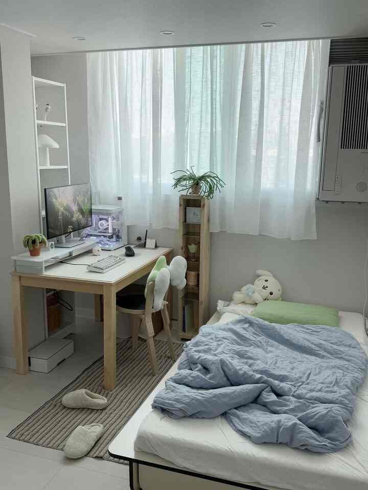 White and natural toned compact single bedroom featuring desk, bed, and plants with cozy atmosphere