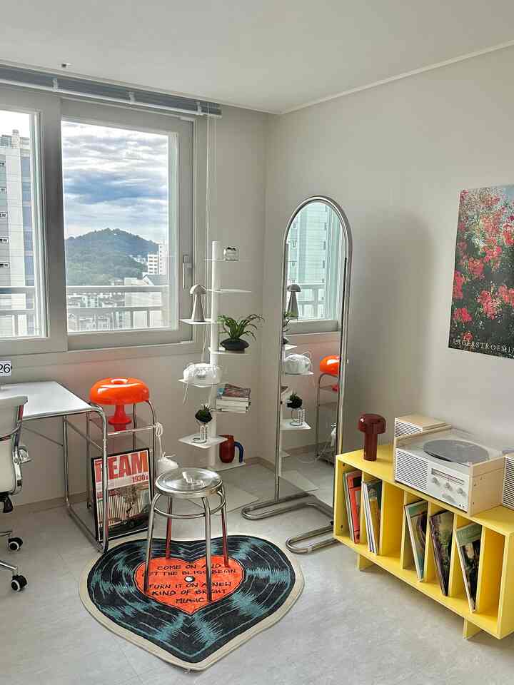 ホワイトとイエローのトーンが特徴のホームオフィス、ミッドセンチュリーモダンのオレンジ照明とLP収納、壁の花のポスターが配された印象的なインテリア