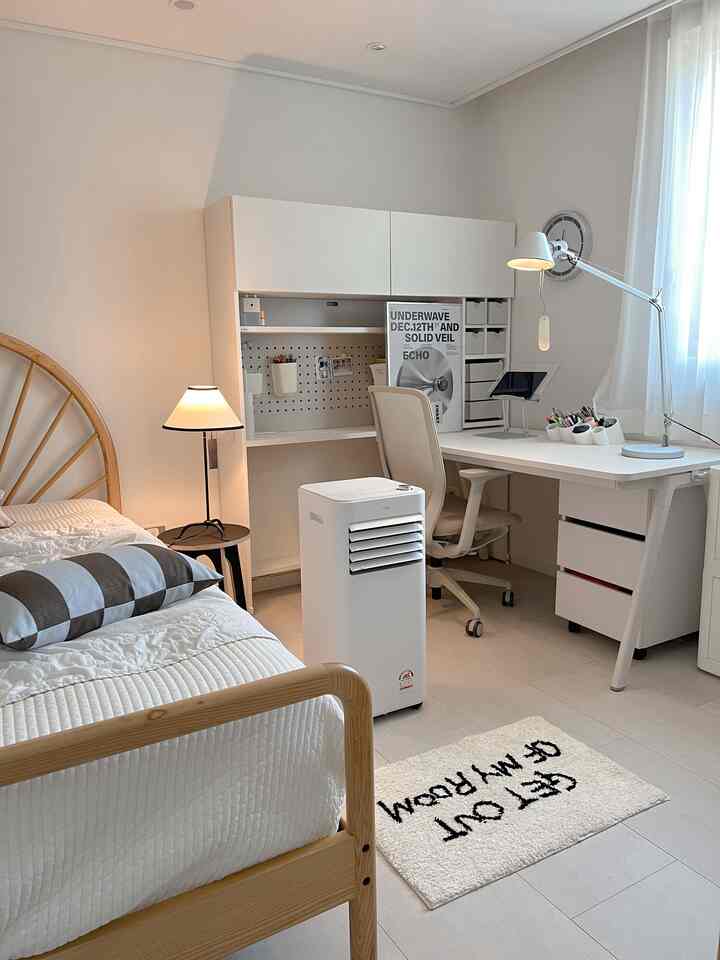 白と木目調が調和した小さな子供部屋、シンプルなデスクとベッド、移動式エアコンが配置された整った学習空間