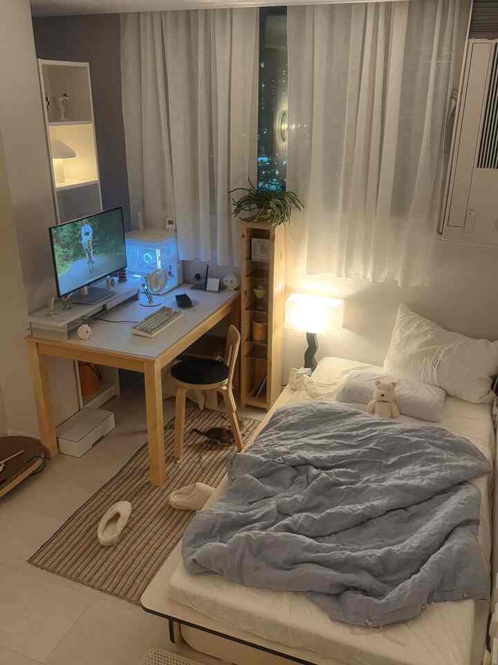 白とナチュラルトーンのワンルーム寝室、机とモニターが配置されたミニマルで居心地の良いホームオフィス空間