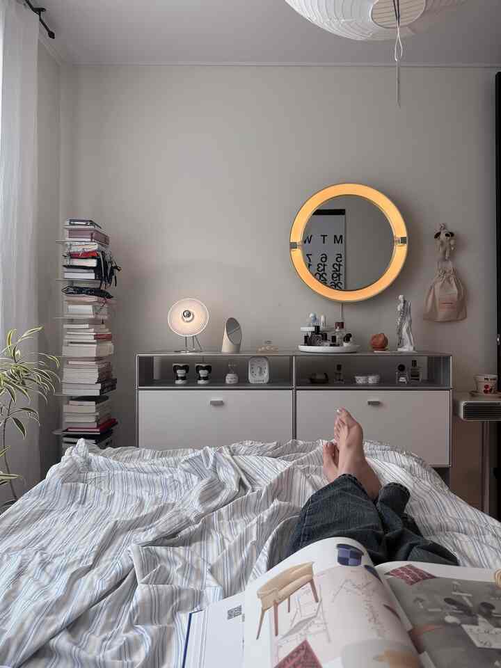 ホワイトの壁と木目調の床がある寝室、中央に丸い照明付き鏡と化粧台が配置された雰囲気のあるインテリア