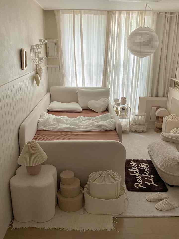 柔らかな白とベージュの色調の寝室、中央に大きなベッドとスツール、カーテンと照明が調和したナチュラルモダンなインテリア