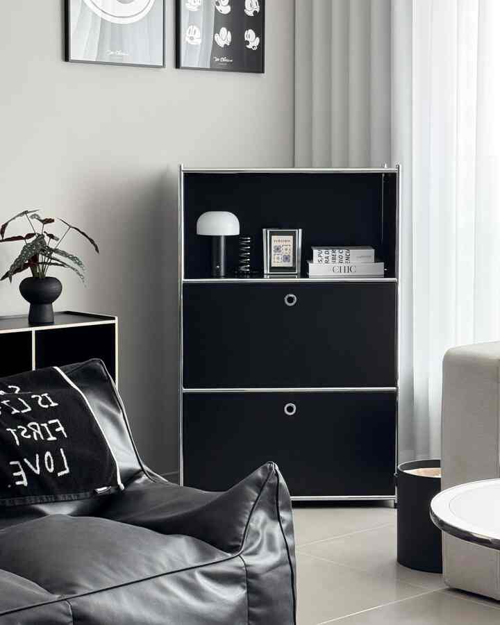 モノトーン調のリビング空間、黒い3段キャビネットが壁際に配置され、ビーンバッグソファと白いカーテンが調和したシンプルモダンなインテリア