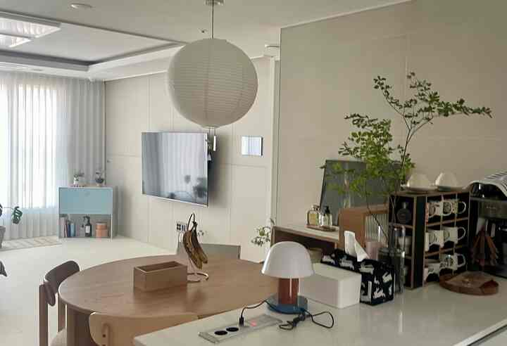 ベージュとホワイトのトーンで統一されたオープンキッチンとダイニングルーム、木製のダイニングテーブルと椅子、ペット用品が配置された自然な雰囲気の空間