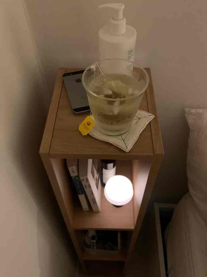 ライトブラウンの木目調隙間収納ナイトテーブル、寝室にあるムードランプとガラスカップが配置された雰囲気のある空間