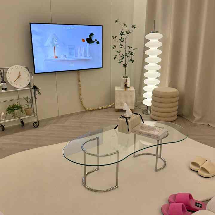 白と木目調の調和が取れたリビング、特徴的なガラスコーヒーテーブルとスツール、フロアランプ、植物が配置された雰囲気のあるインテリア