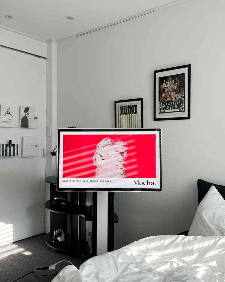 白と黒のトーンの寝室、中央にモニタースタンドと棚が配置された清潔感のある空間